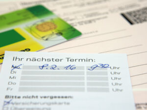 Arzttermin-Erinnerungskarte mit handgeschriebenem Datum und Zeit, daneben eine Krankenversicherungskarte.